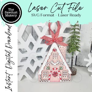 Puede incluir: Adorno navideño de casa de jengibre rosa y blanco con una cinta roja y blanca. El adorno tiene una puerta de bastón de caramelo, ventanas y una chimenea. El texto incluye "Laser Cut File" y "Instant Digital Download".