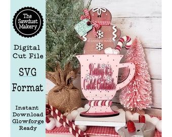 May include: A pink and white wooden mug with the text "Baby it's Cold Outside" and a gingerbread man on top. The mug is sitting on a white wooden base with a red and white checkered background.