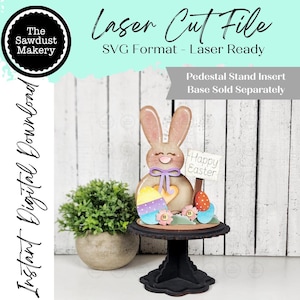 Könnte beinhalten: Eine lasergeschnittene Osterhasenfigur mit einem Schild mit der Aufschrift "Frohe Ostern". Der Hase steht auf einem Podest mit bunten Ostereiern und Blumen. Das Bild enthält auch den Text "Laser Cut File" und "Instant Digital Download".