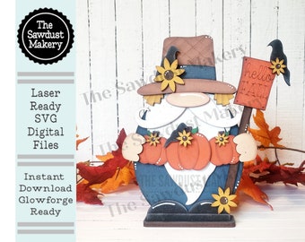 May include: A wooden gnome figurine with a brown hat, a white beard, and a blue shirt. The gnome is holding three pumpkins and a sign that says "hello fall".