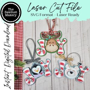 May include: Laser cut Christmas ornaments in the shape of the word "JOY" with festive designs. The ornaments include a reindeer, a penguin, and a polar bear, all with red and white striped accents. The text "Laser Cut File" is visible.