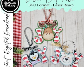 Puede incluir: Adornos navideños cortados con láser con la palabra "ALEGRÍA". Presentan un reno, un pingüino y un oso polar, todos con detalles a rayas rojas y blancas. El texto "Laser Cut File" es visible. Decoraciones navideñas.