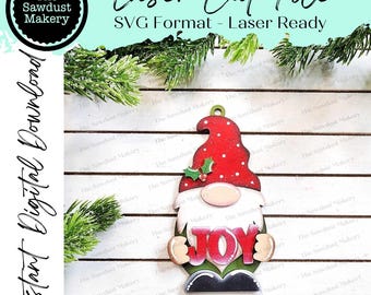 May include: A wooden gnome ornament with a red hat, white beard, and a green holly sprig. The gnome is holding a red, green, and white "JOY" sign.