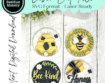 May include: Four round wooden signs with bee-themed designs. The signs feature a beehive, a bee, a wreath of flowers, and the words "Bee Kind" and "Honey".