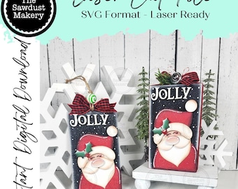 May include: Two wooden Christmas ornaments with Santa Claus designs. Each ornament is rectangular, painted with a black background and the word "JOLLY". One ornament hangs from a twine loop, and the other sits on a small white platform.