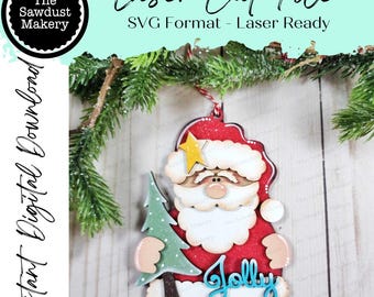 May include: A wooden Christmas ornament depicting Santa Claus holding a green tree. The ornament is red, white, and beige with a yellow star and the word "Jolly" in blue. The text "Laser Cut File" and "Instant Digital Download" are also visible.