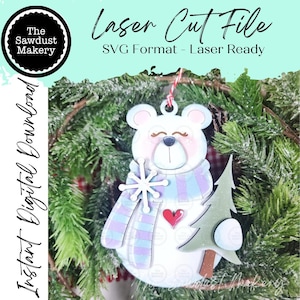 May include: A laser cut file digital download featuring a white bear ornament with a blue and purple striped scarf, a white snowflake, a red heart, and a green pine tree. The text reads Laser Cut File, SVG Format - Laser Ready, and Instant Digital Download.
