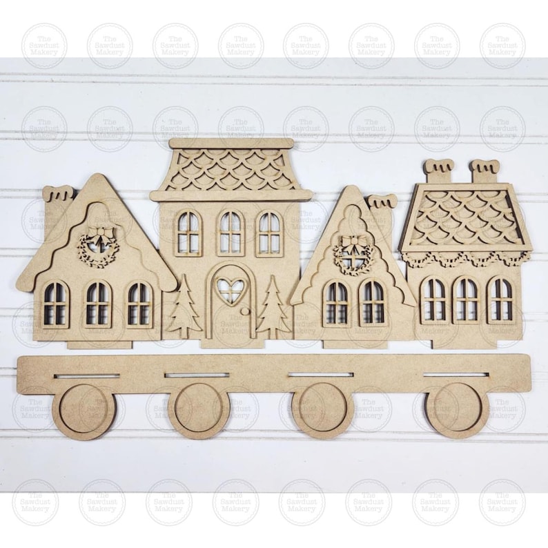 May include: A wooden Christmas village train with four houses and four wheels. The houses have intricate details, including windows, wreaths, and a heart-shaped door. The train is made of light brown wood.