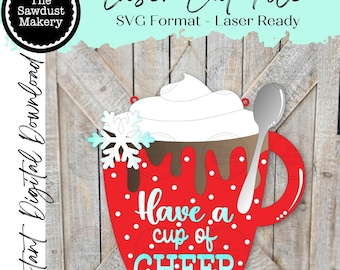 Pode incluir: Um design de arquivo de corte a laser de uma caneca vermelha com chantilly branco, uma colher prateada e um floco de neve. A caneca tem as palavras "Have a cup of CHEER" em branco e azul. Download digital instantâneo.
