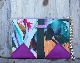 May include: A purple and green clutch with a gold chain. The clutch has a geometric design with a black stripe down the center. The clutch has a label that says "J. Sass & J. Jam".