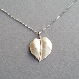 May include: A silver necklace with a hammered leaf pendant. The leaf is a simple, organic shape with a textured surface.
