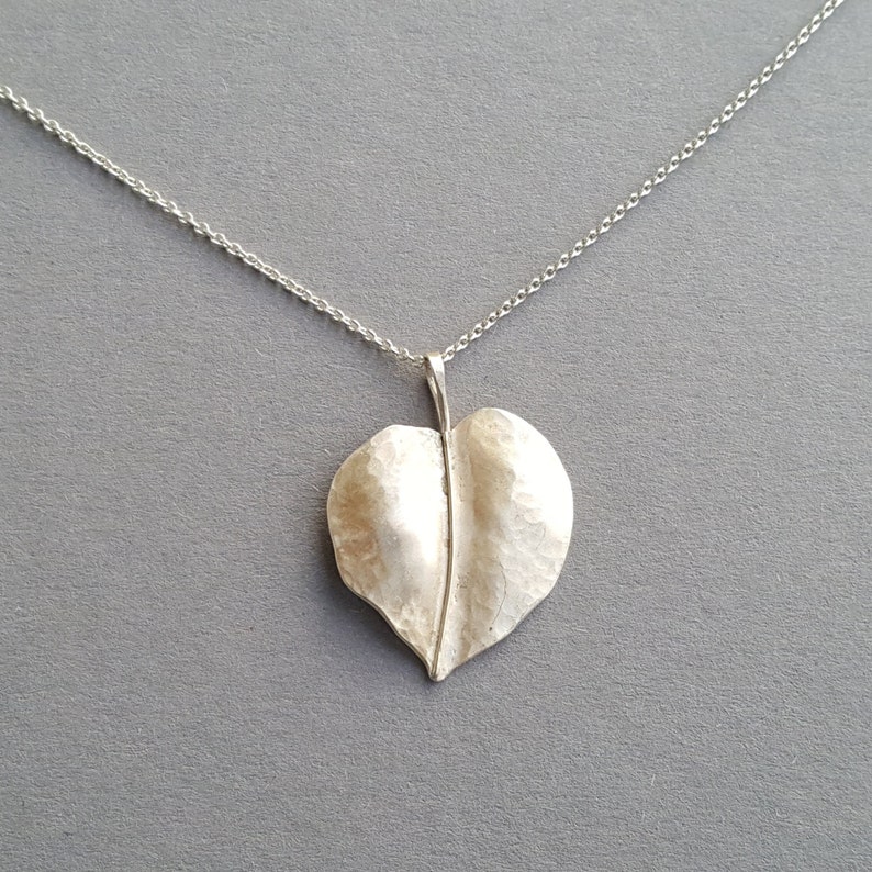 May include: A silver necklace with a hammered leaf pendant. The leaf is a simple, organic shape with a textured surface.