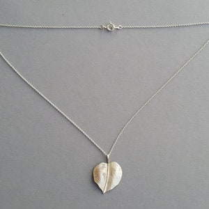 May include: A silver chain necklace with a leaf-shaped pendant. The pendant is textured and has a slightly hammered finish.