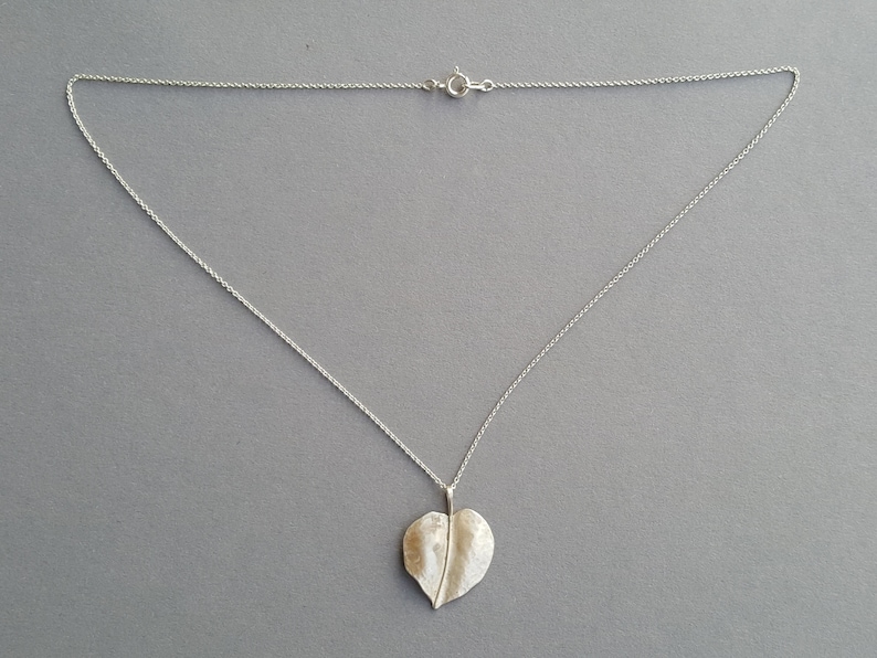 May include: A silver chain necklace with a leaf-shaped pendant. The pendant is textured and has a slightly hammered finish.