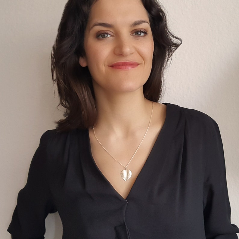 May include: A woman wearing a black shirt with a silver leaf pendant necklace.