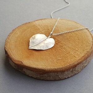 May include: A silver heart-shaped leaf pendant necklace on a silver chain. The pendant has a hammered texture and a delicate vein running down the center.