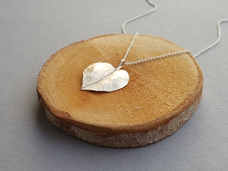 May include: A silver heart-shaped leaf pendant necklace on a silver chain. The pendant has a hammered texture and a delicate vein running down the center.
