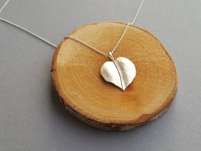 May include: A silver necklace with a heart-shaped leaf pendant. The pendant is textured and has a raised vein down the center.