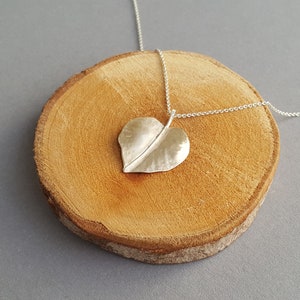 May include: A silver necklace with a hammered heart-shaped leaf pendant. The necklace is displayed on a wooden surface.