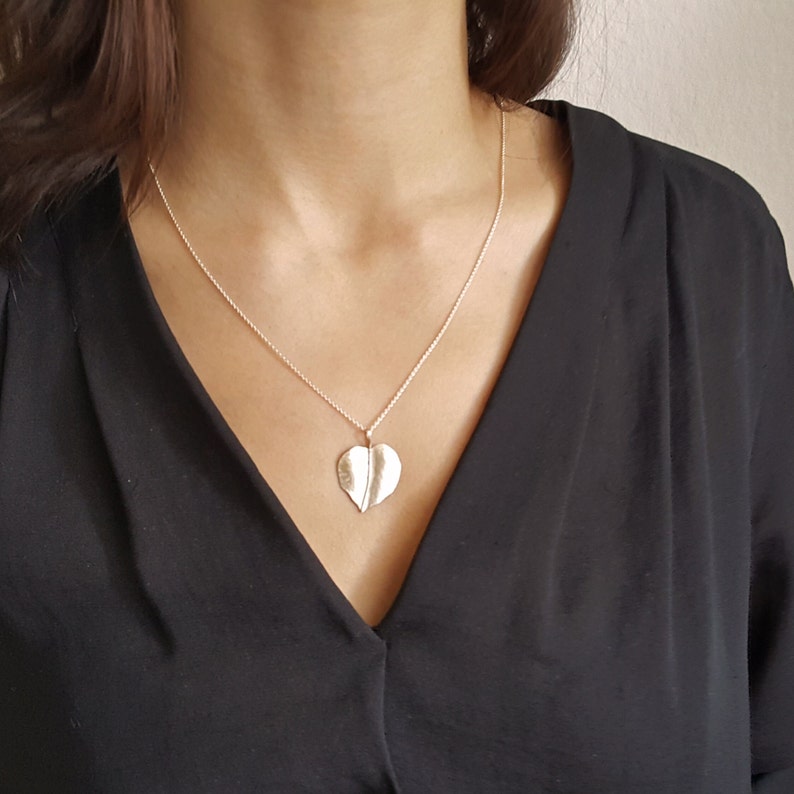 May include: A silver necklace with a heart-shaped pendant. The pendant is made of two leaves that are joined together in the middle.