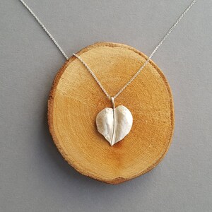 May include: A silver necklace with a heart-shaped leaf pendant. The pendant is textured and has a delicate stem.