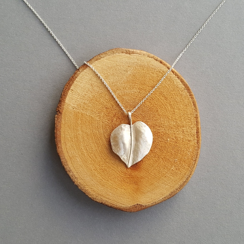 May include: A silver necklace with a heart-shaped leaf pendant. The pendant is textured and has a delicate stem.