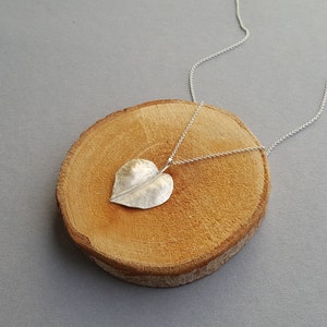 May include: A silver necklace with a hammered leaf pendant. The necklace is displayed on a wooden surface.