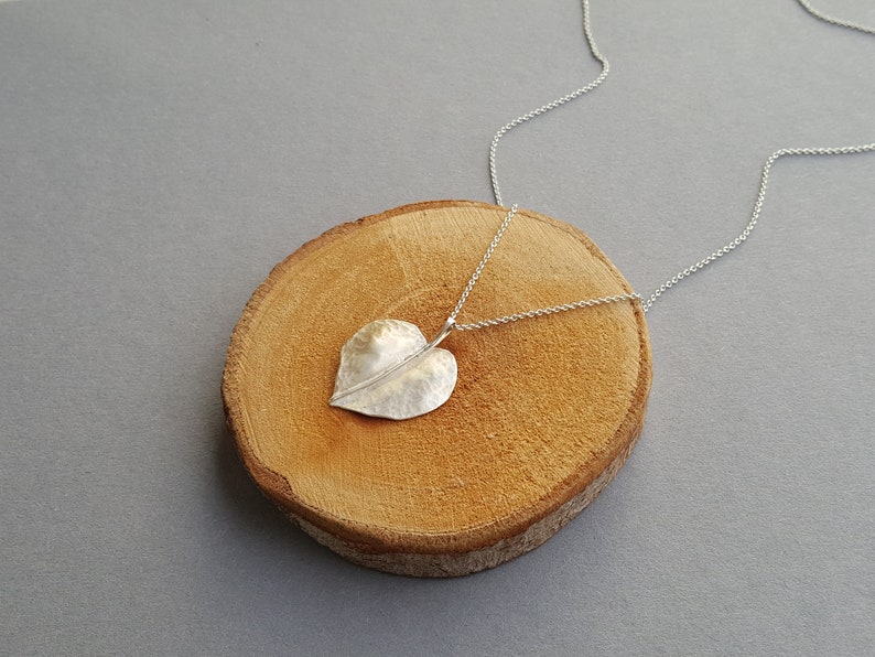May include: A silver necklace with a hammered leaf pendant. The necklace is displayed on a wooden surface.