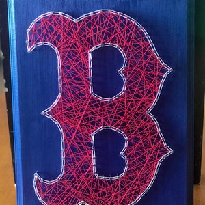 May include: A red and white string art piece of the letter "B" on a dark blue wooden background.