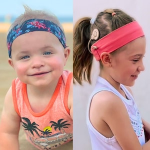 以下が含まれることがあります： 2人の子供がヘアバンドを着用しています。一人は赤と青のスーパーヒーローのデザインのネイビーブルーのヘアバンドを着用しています。もう一人はピンクのヘアバンドを着用しています。左の子供はヤシの木のデザインのオレンジ色のタンクトップを着ています。