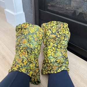 May include: A pair of green and yellow floral leg warmers made of silk. The leg warmers are worn over black leggings.