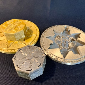 以下が含まれることがあります： エジプトの象形文字が施された、装飾的な金属製のパズルボックス3つ。一番大きいものは金色で、星型のデザインと、上に小さな八角形の箱があります。他の2つは銀色と灰色で、複雑な幾何学模様が施されています。
