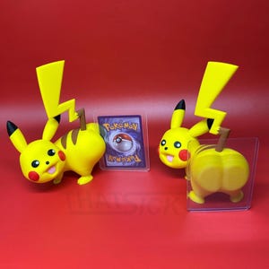 May include: Two yellow Pikachu figurines with black-tipped ears, red cheeks, and lightning bolt tails. One figure faces forward while the other shows its back. A small rectangular trading card with a Pokeball graphic is displayed between them.