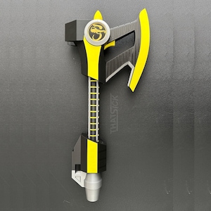 May include: A black, yellow, and silver axe prop with a circular emblem. The axe head and handle feature yellow accents. The text "THAT SICK" is printed on the handle. The axe is likely a prop or toy.
