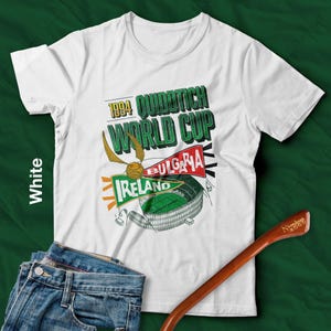 May include: White t-shirt with a graphic design featuring the text "1994 Quidditch World Cup" and the flags of Ireland and Bulgaria. The design includes a golden snitch and a stadium illustration. A wooden wand and blue jeans are also in the image.