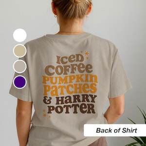 May include: Beige t-shirt with the text "Iced Coffee, Pumpkin Patches & Harry Potter" in brown and orange lettering. The shirt has a crew neck and short sleeves. The words are arranged vertically.