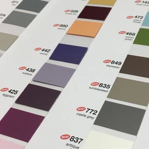 May include: Color swatches arranged diagonally, showcasing a variety of hues. The palette includes shades of gray, purple, orange, and brown, with labels indicating color names and numbers. Some swatches are marked with "NEW!"