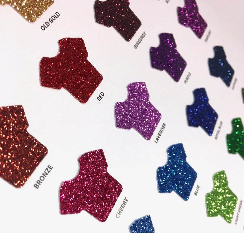 May include: A variety of glitter colors in the shape of a t-shirt. The colors include old gold, red, bronze, cherry, burgundy, lavender, blue, royal blue, and lime green.