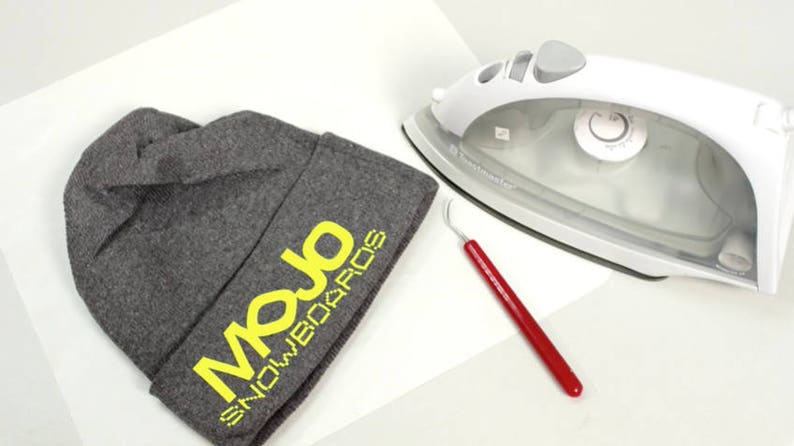 May include: A gray beanie with the yellow text "Mojo Snowboards" on the side. An iron and a red tool are also in the image.