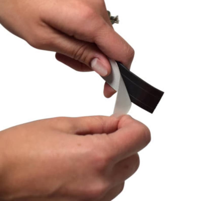 Pu&ograve; includere: Una mano sta rimuovendo il rivestimento protettivo da un rotolo di nastro magnetico nero.