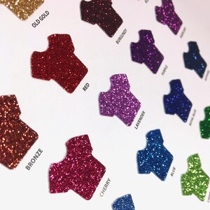 May include: A range of glitter colours in the shape of a t-shirt. The colours include old gold, red, bronze, cherry, burgundy, lavender, blue, royal blue, and lime green.