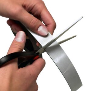 Pu&ograve; includere: Una persona sta usando un paio di forbici nere per tagliare un rotolo di nastro magnetico argentato.