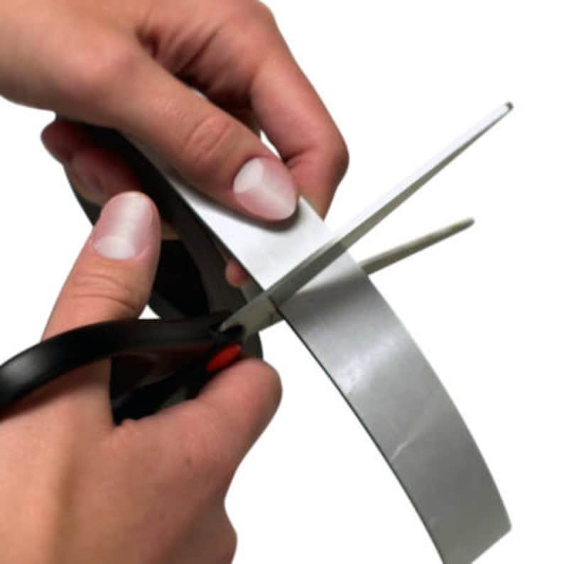 Pu&ograve; includere: Una persona sta usando un paio di forbici nere per tagliare un rotolo di nastro magnetico argentato.