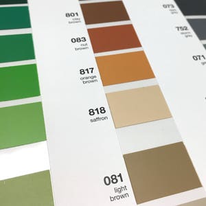 May include: A color chart with various shades of brown, green, and gray. The chart includes color swatches labeled with numbers and names like "nut brown," "orange brown," and "saffron." The image is well-lit, showcasing the different hues and tones.