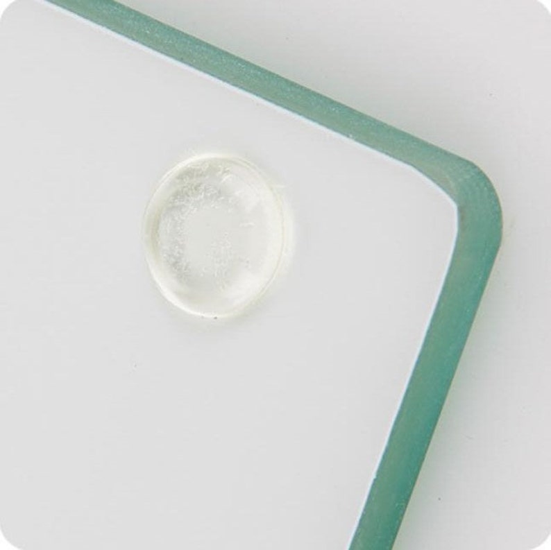 May include: A close-up of a clear glass cutting board with a round, clear rubber bumper on the bottom.