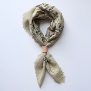 May include: A light green bandana with a black floral print and a brown leather tie. The bandana is tied around the neck and the ends are hanging down.