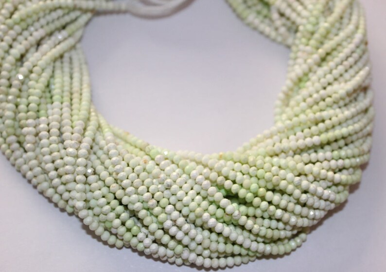 May include: A collection of small, round, pale green beads. The beads are closely strung, forming a textured, flowing display. The beads have a gentle sheen, reflecting light. The overall effect is delicate and elegant, ideal for jewellery making.