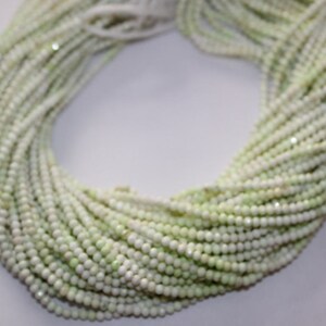 May include: A large bundle of small, round, pale green beads. The beads are strung together, forming multiple strands that are intertwined. The beads have a slightly iridescent quality, reflecting light. The overall effect is delicate and elegant.