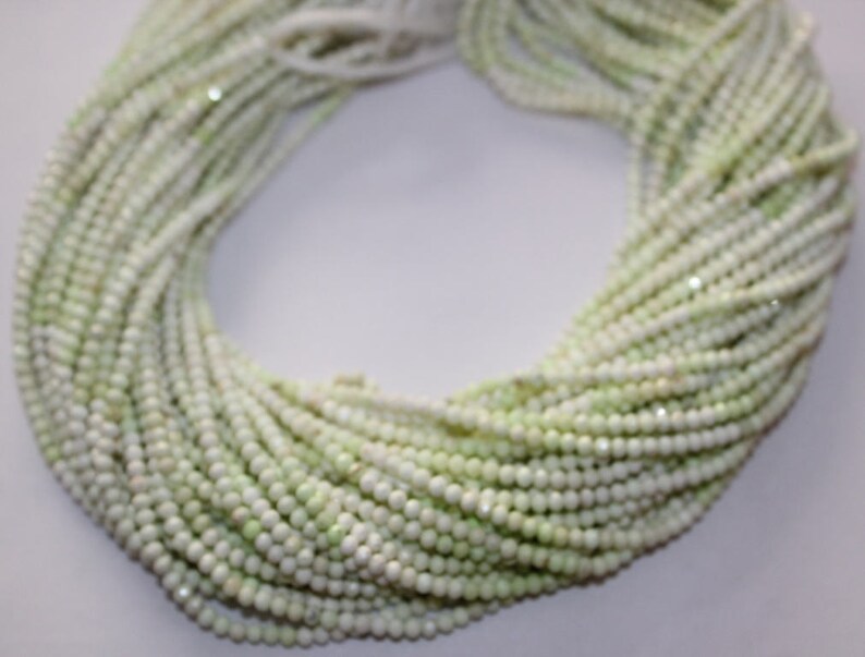 May include: A large bundle of small, round, pale green beads. The beads are strung together, forming multiple strands that are intertwined. The beads have a slightly iridescent quality, reflecting light. The overall effect is delicate and elegant.