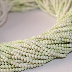 May include: Close-up of a collection of light green, faceted beads. The beads are strung together, forming multiple strands. The beads have a subtle sheen and are arranged in a circular pattern, suggesting they are ready for jewelry making.